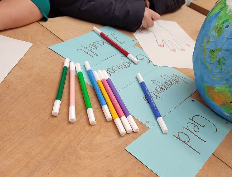 Workshop-Szene des GloW Karlsruhe e.V., Kinder beschriften Zettel, daneben liegt ein selbstgebastelteter Globus in blau und grün 