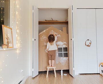 Kind, das ein Papphaus bemalt