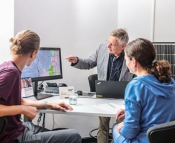 Foto von Menschen am Schreibtisch, die gemeinsam auf Bildschirm schauen