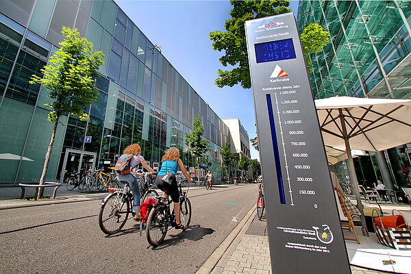 Zwei Radfahrende fahren am Radzähler in Karlsruhe vorbei
