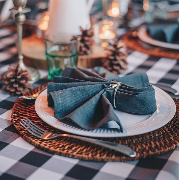 Festlich gedeckter Tisch in Petrol- und Grüntönen mit Stoffservietten und Zapfen als Deko