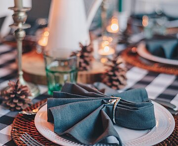 Festlich gedeckter Tisch in Petrol- und Grüntönen mit Stoffservietten und Zapfen als Deko