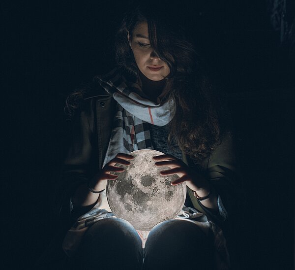 Weiblich gelesene Person in der Dunkelheit hält leuchtenden Globus in den Händen.