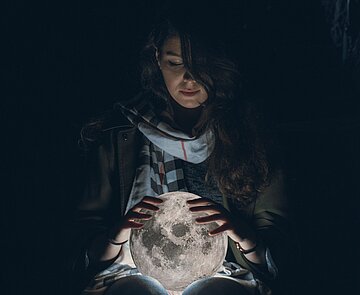 Weiblich gelesene Person in der Dunkelheit hält leuchtenden Globus in den Händen.