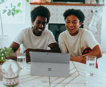 Zwei Personen schauen auf ein Tablet. Sie sehen fröhlich aus.