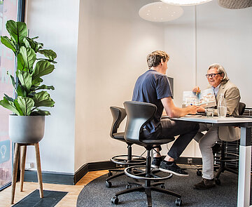 Foto von Büro mit Schreibtisch, an dem zwei Menschen sitzen