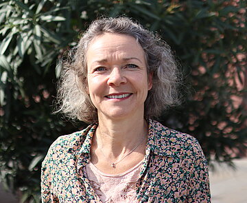 Porträt von Kerstin Bellm, lächelnde Frau vor Oleander-Busch