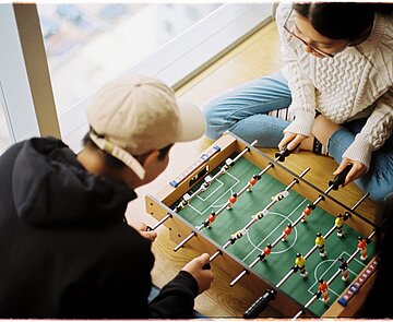 Zwei Personen, die Mini-Tischkicker im Sitzen spielen