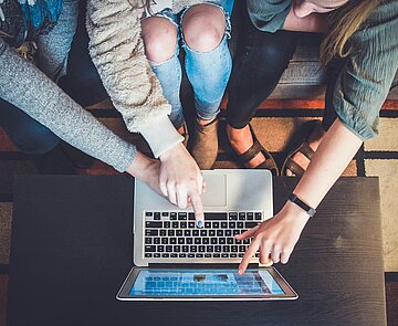 Man sieht aus der Vogelperspektive, wie drei Personen gemeinsam vor einem Laptop sitzen