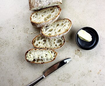 Ein aufgeschnittenes Brot, welches mit Butter oder Margarine bestrichen wird.