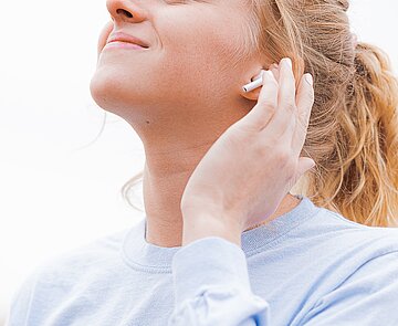 Blonde Frau, die lächelnd über Kopfhörer Musik hört