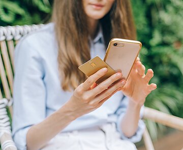 Frau im Grünen auf einem Stuhl sitzend mit Handy und Smartphone in der Hand