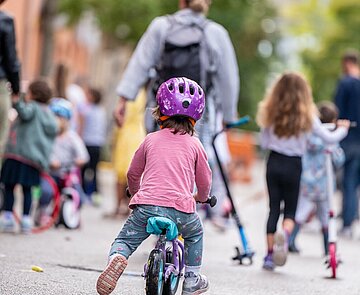 Kind mit Helm fährt auf Laufrad über Straße