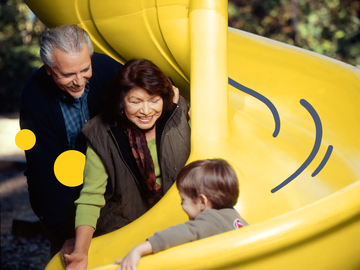 Älteres Paar empfängt Kind am Ende einer gelben Rutsche, blaue Striche als Illustration und gelbe Sphären auf dem Bild (ergänzend)