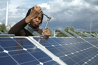 Frau mit Schraubenschlüssel an einer Solarpaneele arbeitend