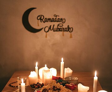 Ein festlich gedeckter Tisch im Kerzenlicht. An der Wand hängt ein Schild mit den Worten "Ramadan Mubarak".