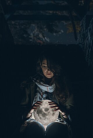 Weiblich gelesene Person in der Dunkelheit hält leuchtenden Globus in den Händen.
