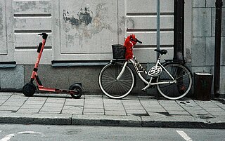 Eine E-Roller und ein Fahrrad lehnen hinter einander an einer Hauswand