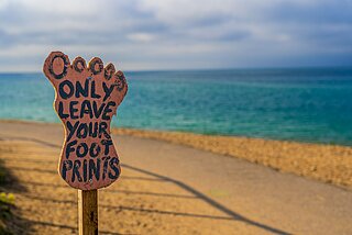 Schild in Form eines Fußabdrucks an einem Strandweg, Aufschrift in aufgeschriebenen Lettern: Only leave your footprints