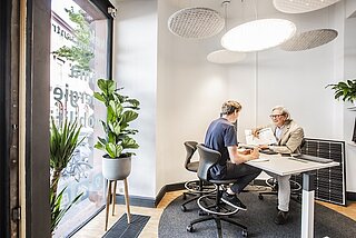 Zwei Personen im KEK Beratungszentrum, ein Mann lässt sich beraten, eine Mitarbeiterin der KEK berät, es ist ein heller Raum mit Topfpflanzen