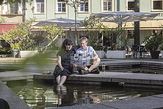 Zwei Menschen am Brunnen in Karlsruhe mit dem Stadtplan für heiße Tage