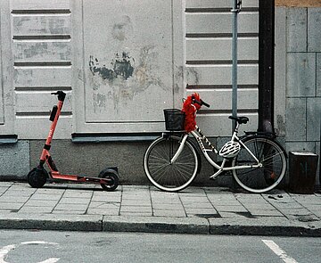 Eine E-Roller und ein Fahrrad lehnen hinter einander an einer Hauswand