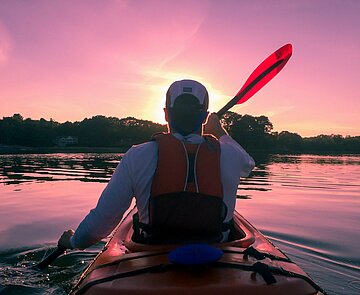Mann im Kayak, der auf einem See dem Sonnenuntergang entgegen paddelt