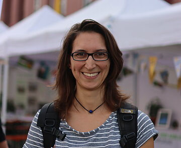 junge Frau auf Karlsruher Marktplatz, die KA°-Materialien lächelnd in Richtung Kamera hält