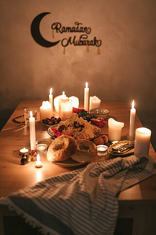 Ein festlich gedeckter Tisch im Kerzenlicht. An der Wand hängt ein Schild mit den Worten "Ramadan Mubarak".